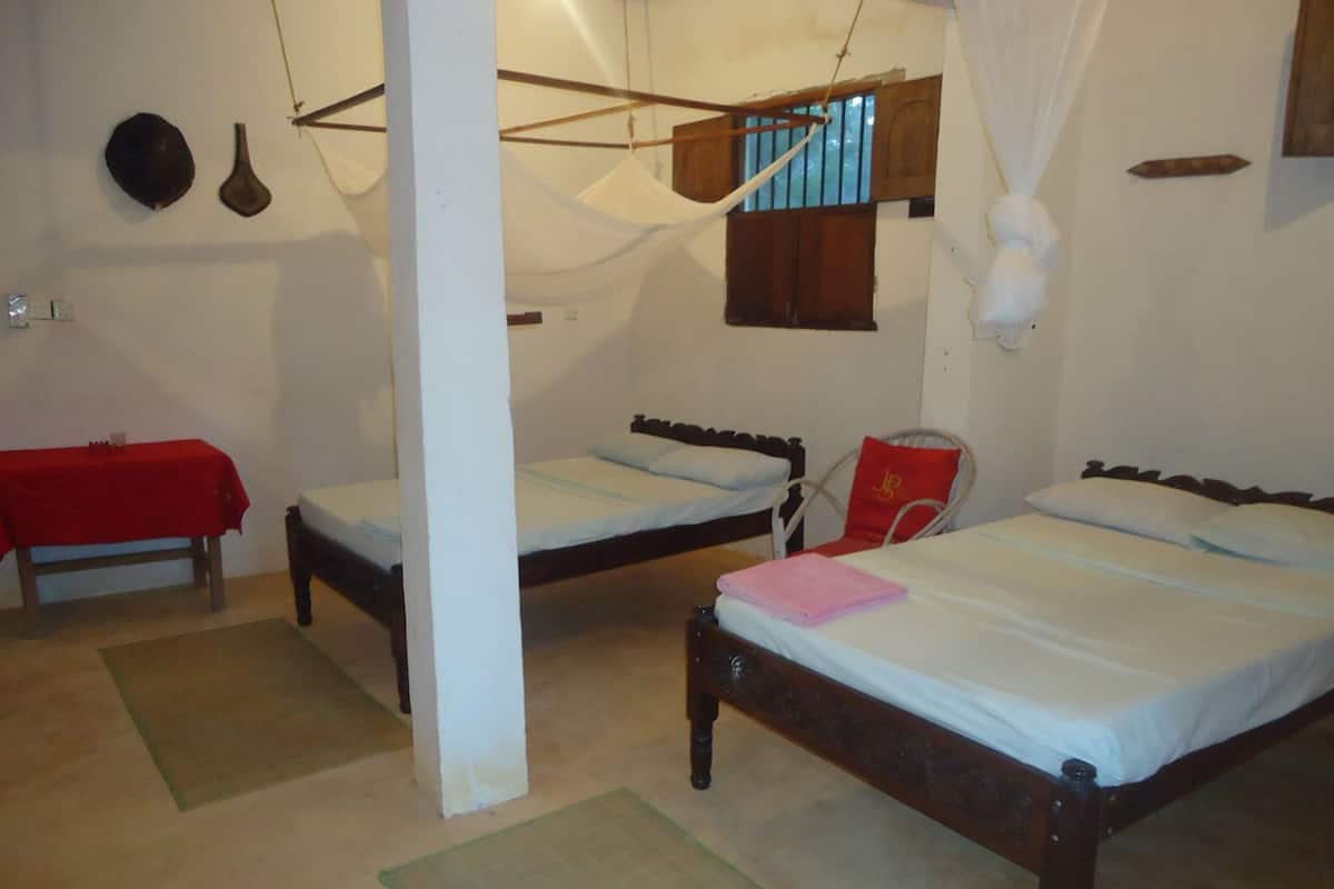 A room with two wooden beds, a red table, and a white pillar.
