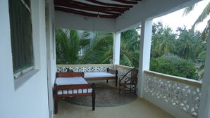 A balcony with a bed, a chair, and a view of palm trees. - Dudu Villas N Backpackers (Lamu)