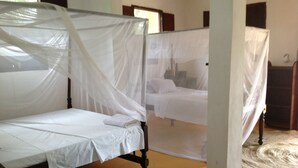 A room with a bed covered by a white canopy, another bed in the background, and a woven rug on the floor. - Dudu Villas N Backpackers (Lamu)