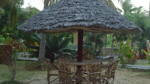 A thatched-roof outdoor dining area with wicker chairs and a central table. - Dudu Villas N Backpackers (Lamu)