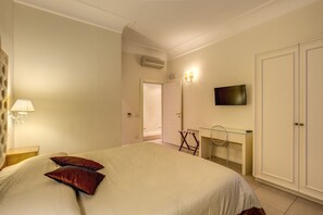 A bedroom with a bed, pillows, a bedside lamp, a TV, a wardrobe, and a desk with a chair. - Luxury apartment in the historic center. (Roma)