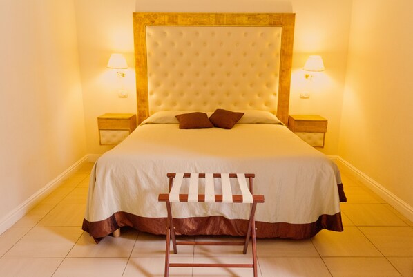 A neatly made bed with a wooden headboard, two bedside lamps, and a wooden rack in front of it. - Luxury apartment in the historic center. (Roma)