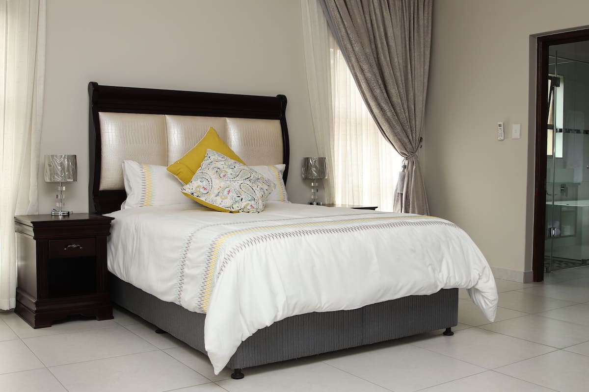 A neatly made bed with a white and gray color scheme, a wooden headboard, and two bedside lamps.