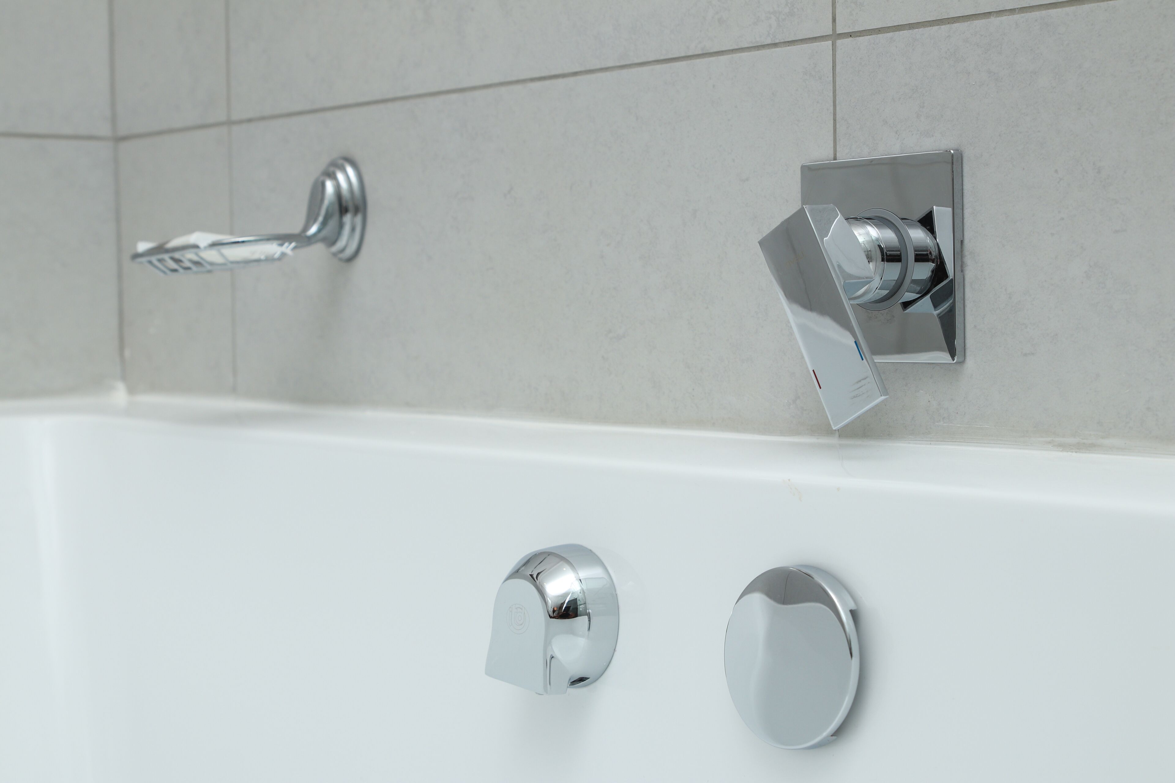 A modern bathroom with a white bathtub, chrome fixtures, and tiled walls.
