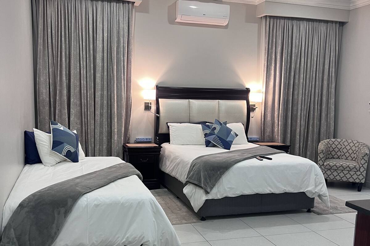 A hotel room with two beds, a nightstand, a chair, and an air conditioning unit.