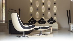 A modern living room with a sofa, two lounge chairs, and a decorative wall with lights. - Letsatsing Lodge (Rustenburg)