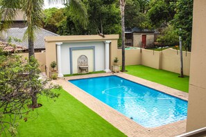 A rectangular swimming pool with a clear blue water surface, surrounded by a well-maintained green lawn and a beige wall.