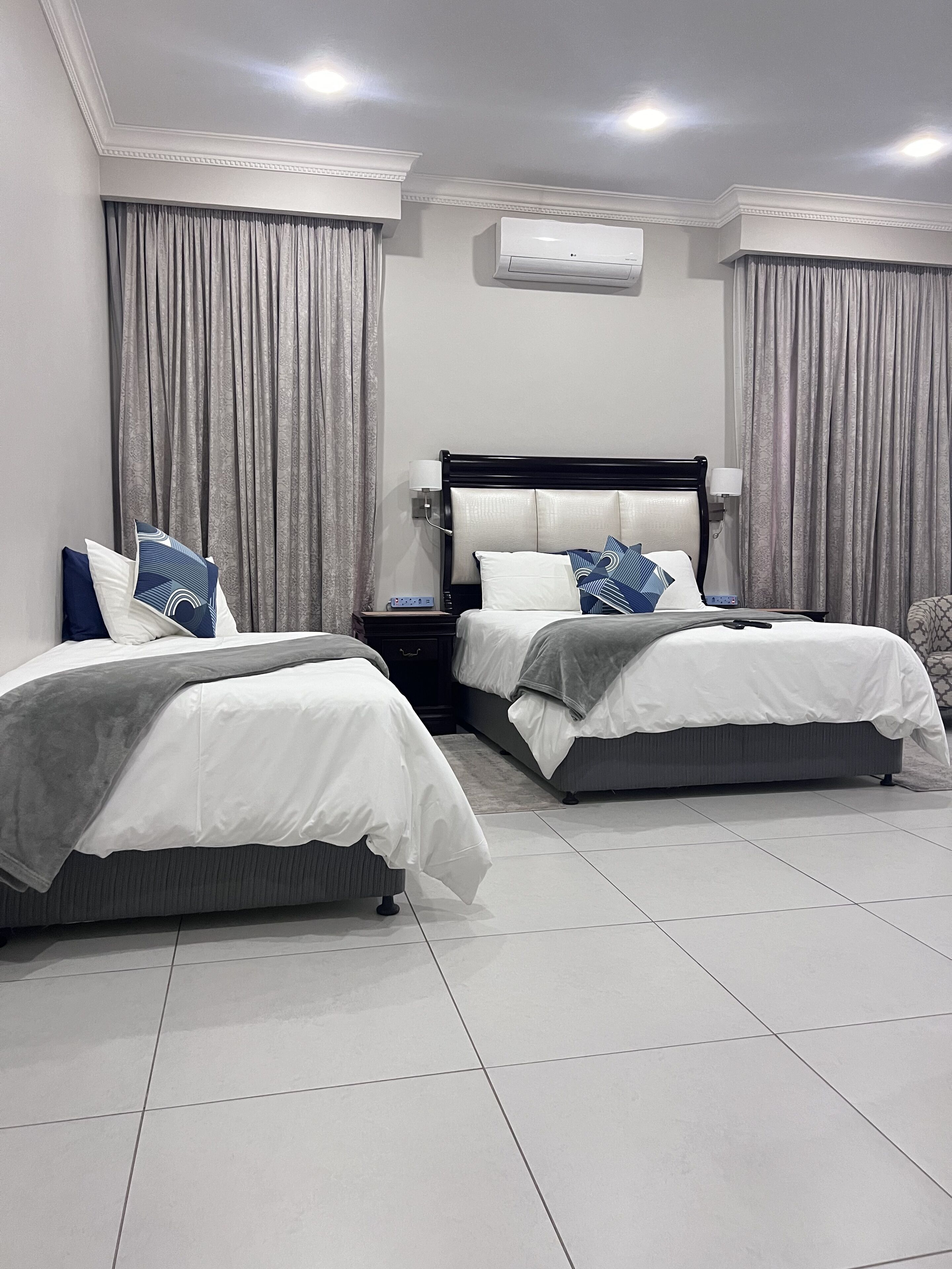 Een hotelkamer met twee bedden, een nachtkastje, een airconditioner en een raam met gordijnen.