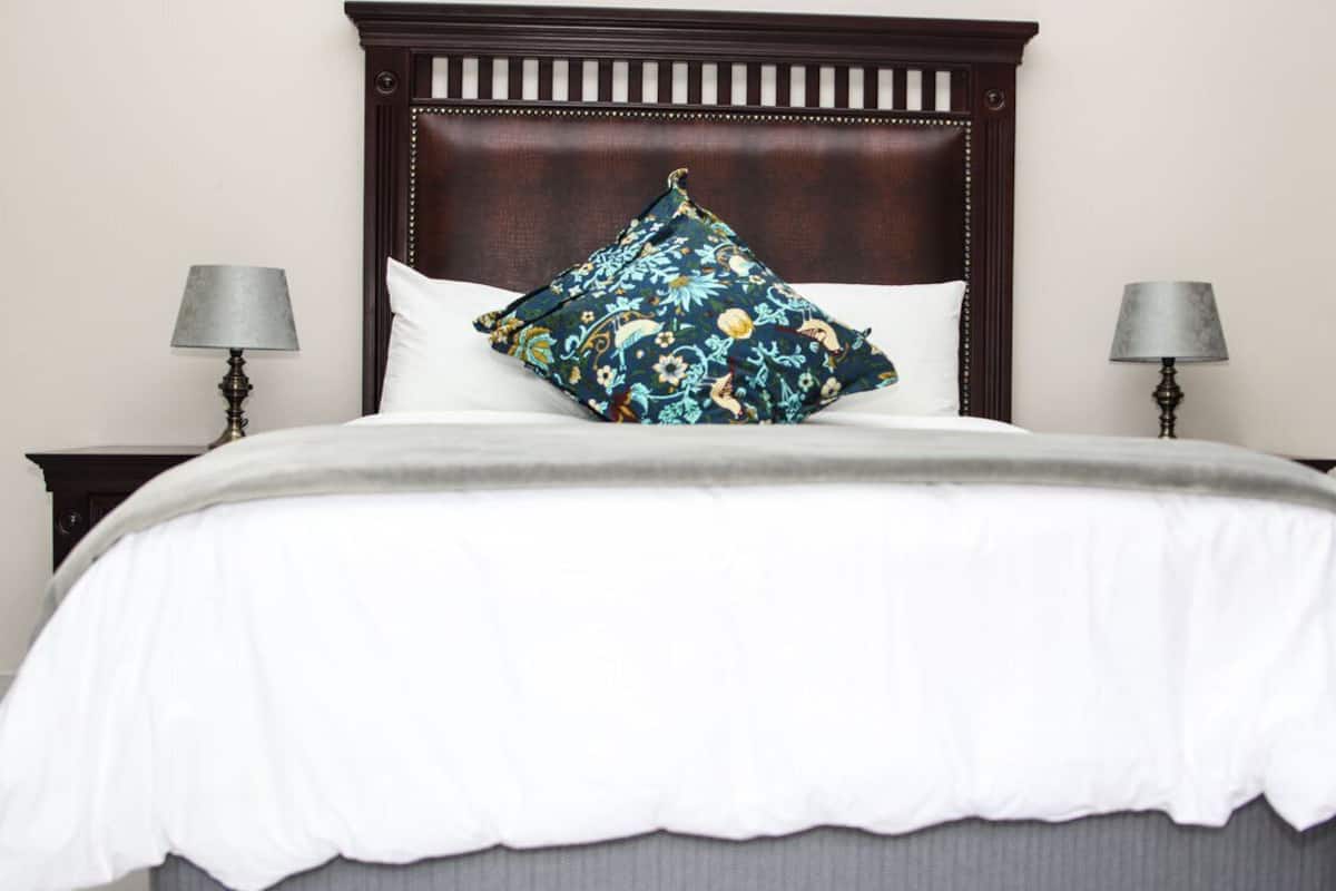 A neatly made bed with a white duvet and a decorative pillow, flanked by two bedside lamps on wooden nightstands.