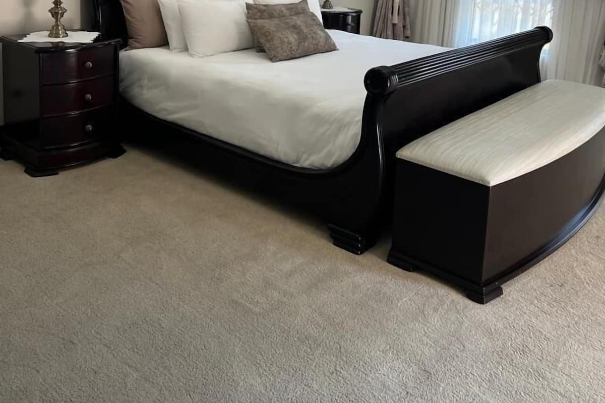 A bedroom with a bed, nightstands, a bench, and a window with curtains.