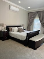 A bedroom with a bed, nightstands, a bench, and a window with curtains.