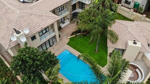 A multi-story building with a swimming pool surrounded by lush greenery and a covered patio area. - Letsatsing Lodge (Rustenburg)