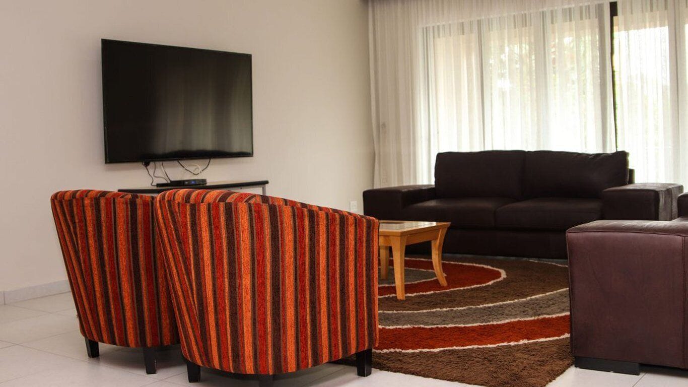 Una sala de estar con una televisión de pantalla plana, dos sillones a rayas, un sofá oscuro y una pequeña mesa de centro de madera.