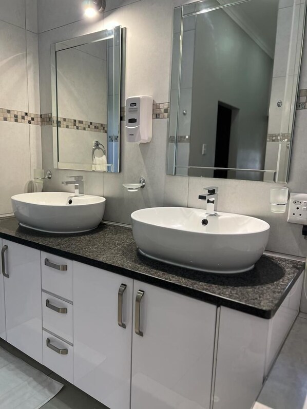 A modern bathroom with two white sinks, a large mirror, and a soap dispenser.