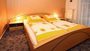 Uma cama de casal com roupa de cama floral, uma mesinha de cabeceira com abajur e uma janela com cortinas.