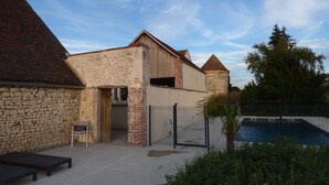 Un bâtiment en pierre avec une extension en briques, une entrée fermée par un portail et un espace piscine.