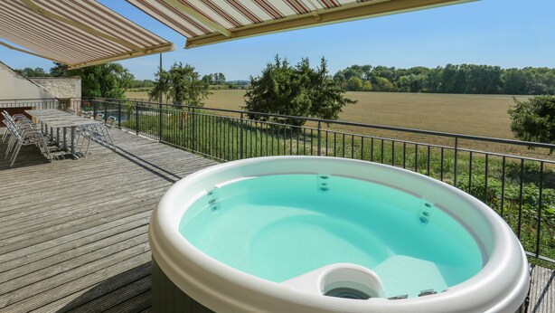 Un bain à remous sur une terrasse en bois, avec vue sur un champ et des arbres.