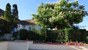 Un bâtiment blanc, doté d’un toit en tuiles, entouré d’une végétation luxuriante et de plantes en fleurs.