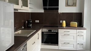 Eine moderne Küche mit weißen Schränken, einem Backofen von Bosch, einem Geschirrspüler und einer Kaffeemaschine.