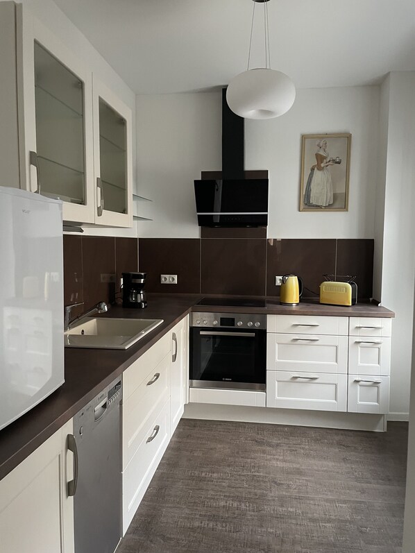 Una cocina moderna con armarios blancos, horno Bosch, lavavajillas y cafetera.