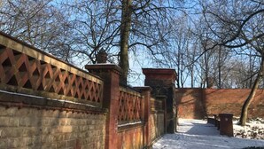 Ein verschneiter Weg mit einer Ziegelmauer und Gitterwerk, der zu einem Tor führt.