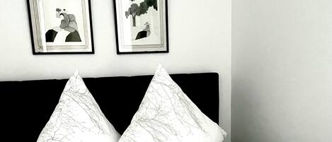 A neatly made bed with a patterned bedspread and two pillows, a folded white towel, and two framed pictures on the wall above the bed.