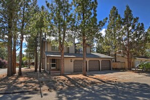 A two-story house with a garage, surrounded by tall pine trees.