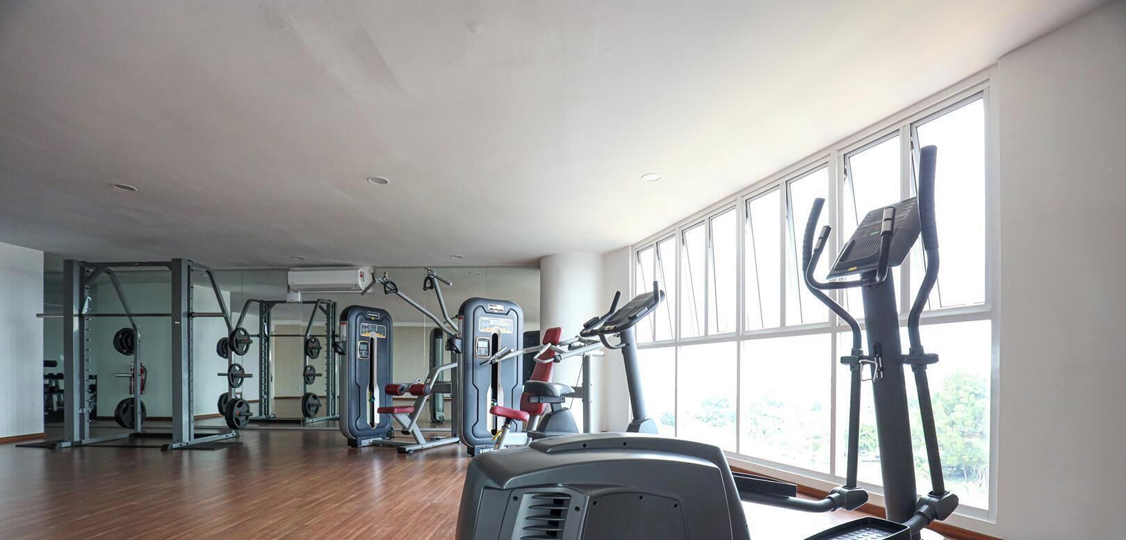 Uma academia com máquinas de cardio, equipamentos de musculação e grandes janelas.