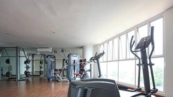 Uma academia com máquinas de cardio, equipamentos de musculação e grandes janelas.