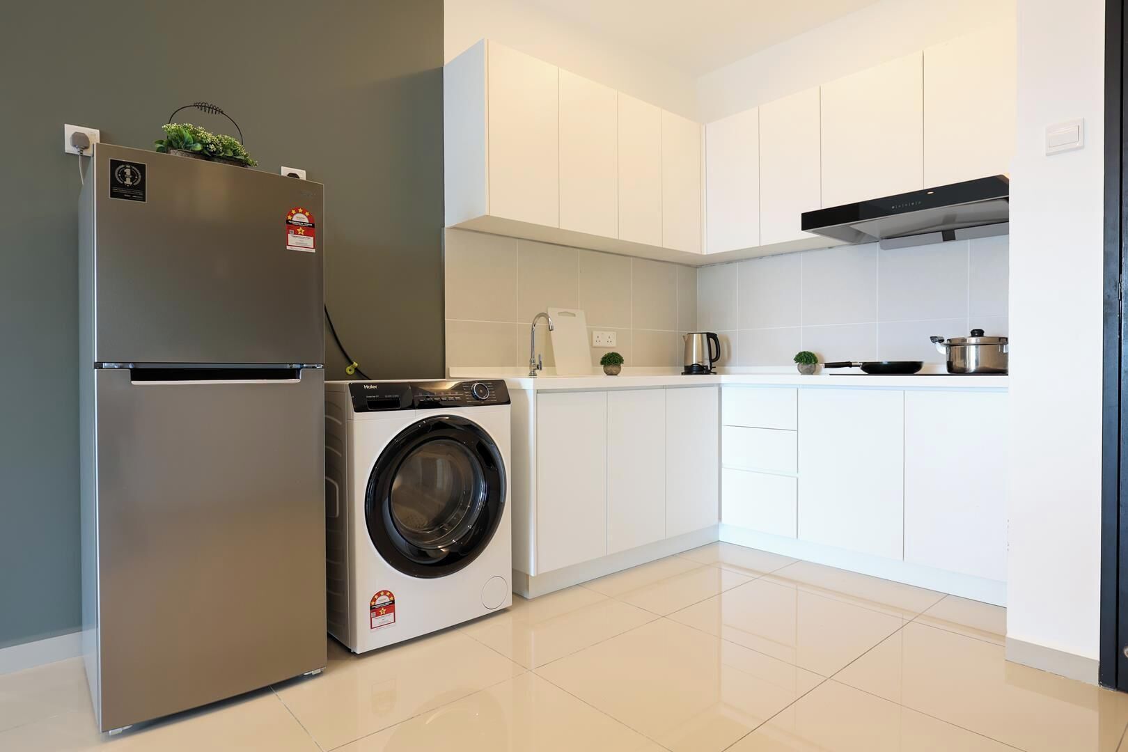 A modern kitchen with a stainless steel refrigerator, a built-in washing machine, white cabinets, and a black range hood.