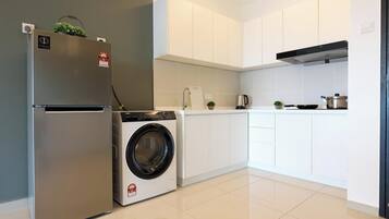 A modern kitchen with a stainless steel refrigerator, a built-in washing machine, white cabinets, and a black range hood.