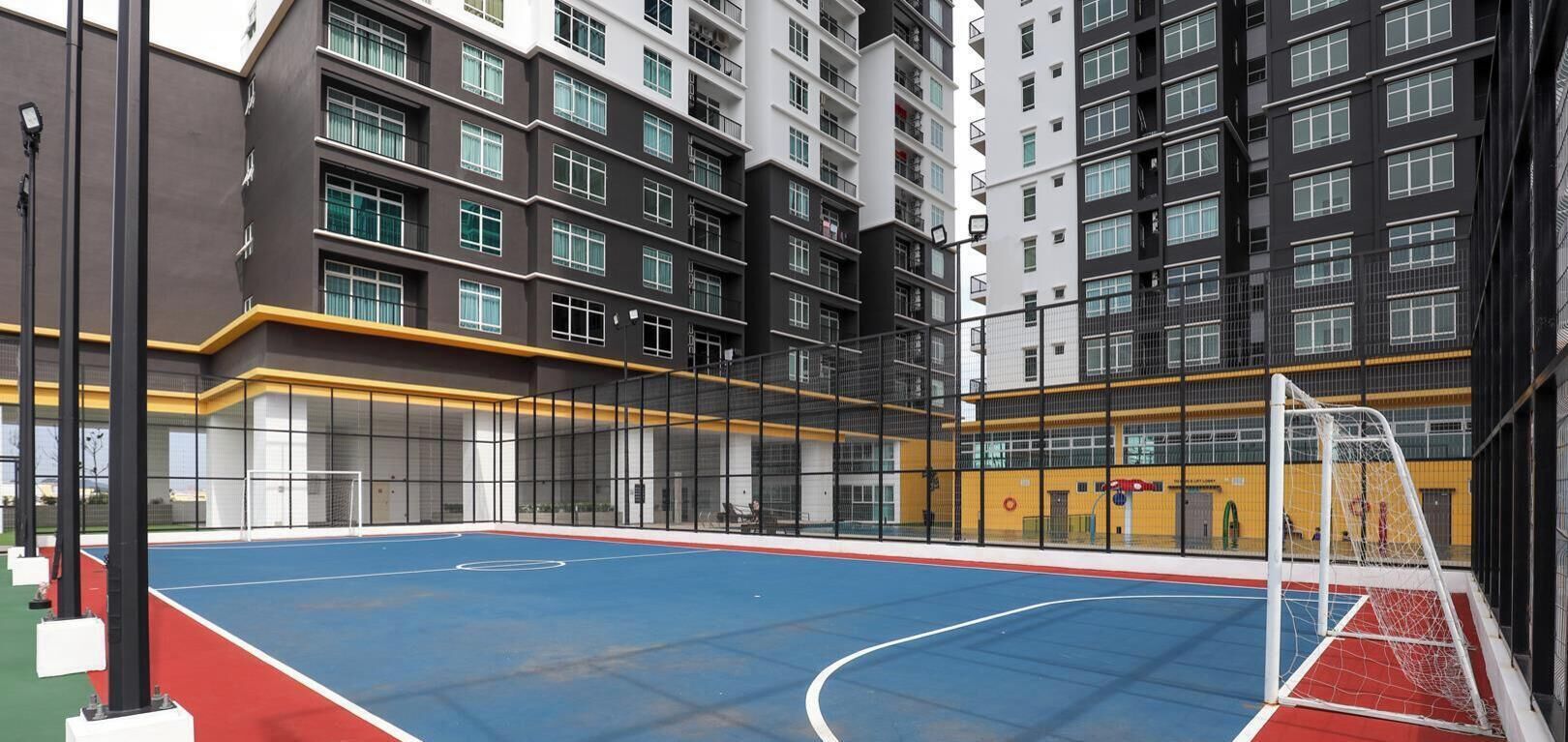 Uma quadra de basquete coberta com uma cesta, cercada por um edifício alto com vários andares e varandas.