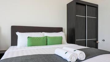 A hotel room with a bed, pillows, a dark wardrobe, and a rolled towel on the bed.