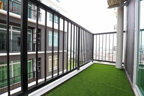 Un balcon avec une balustrade noire, un petit coin d’herbe artificielle et une vue sur le paysage urbain.