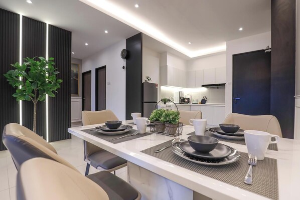 Un espace repas moderne avec une table blanche dressée pour quatre personnes, entourée de chaises de couleur beige.