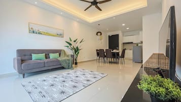 A modern living room with a sofa, dining table, and chairs, a ceiling fan, and a kitchen area in the background.