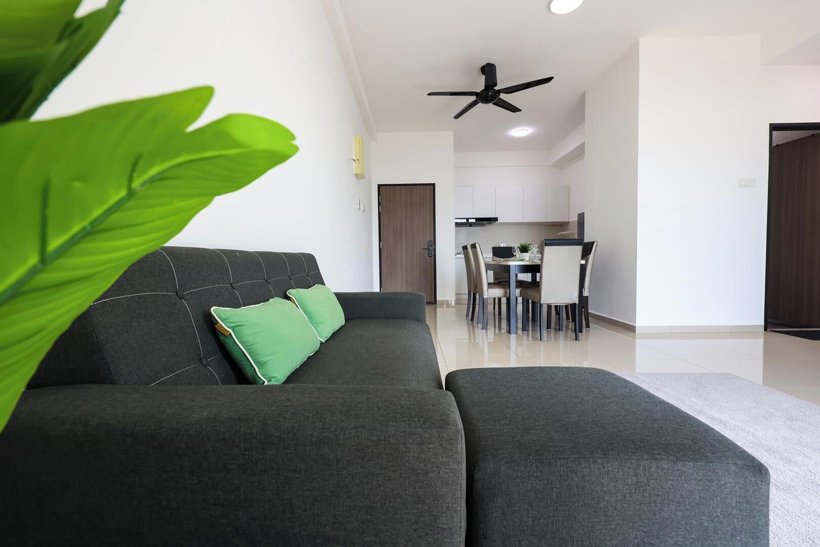 A modern living room with a sofa, green cushions, a dining area with a table and chairs, and a ceiling fan.