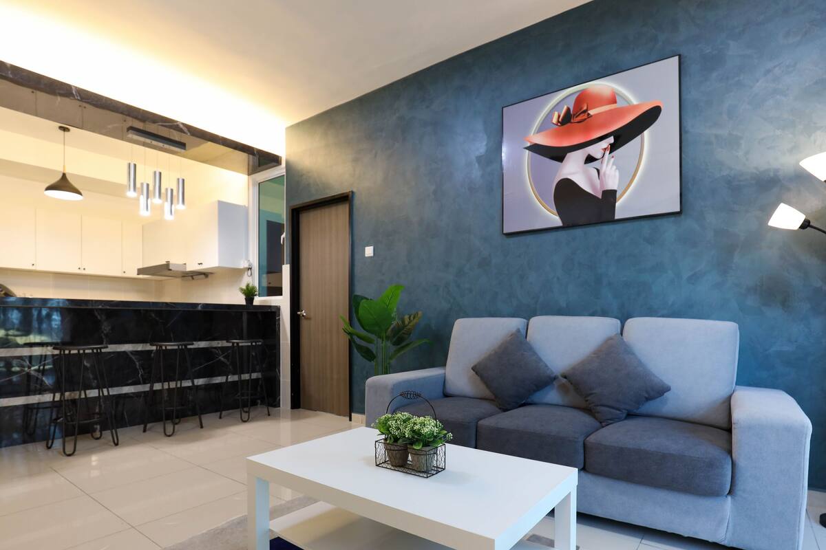 A modern living room with a grey sofa, a white coffee table, and a kitchen area with a black marble countertop and white cabinets.