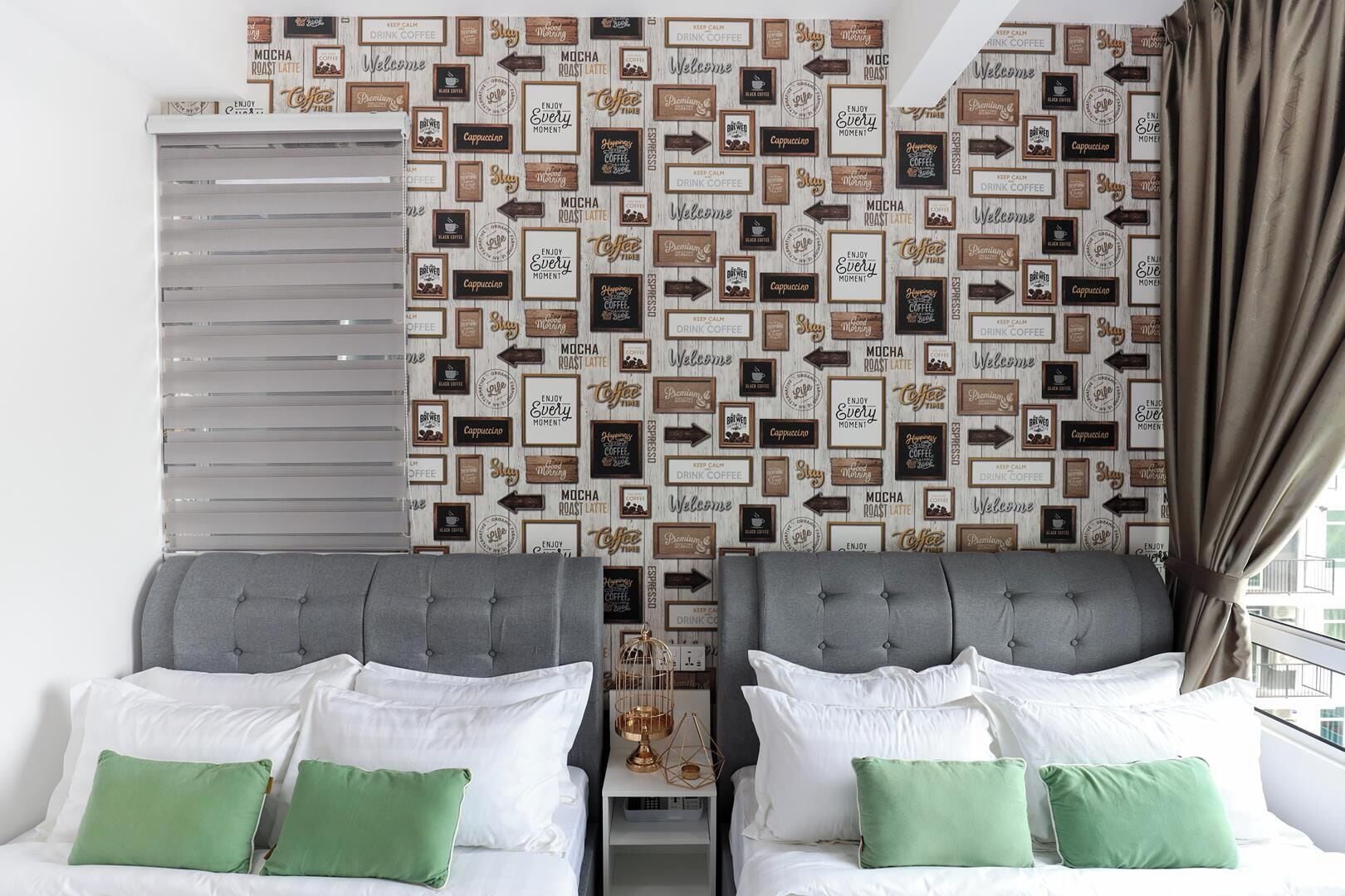 A hotel room with two beds, a window with blinds, and a wall decorated with coffee-themed signs.