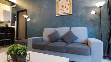 A modern living room with a grey sofa, two floor lamps, a framed artwork, and a small table with a plant.