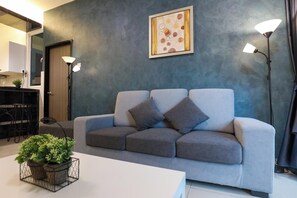 Un salon moderne avec un canapé gris, deux lampadaires, une œuvre d’art encadrée et une petite table sur laquelle est posée une plante.