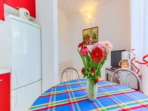 Un comedor con mantel colorido, un florero con flores, una cafetera y un televisor.