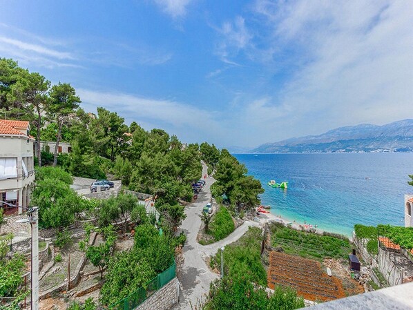 A coastal village with a narrow road leading to a beach, surrounded by greenery and traditional buildings. - Apartments Ivo (Postira)