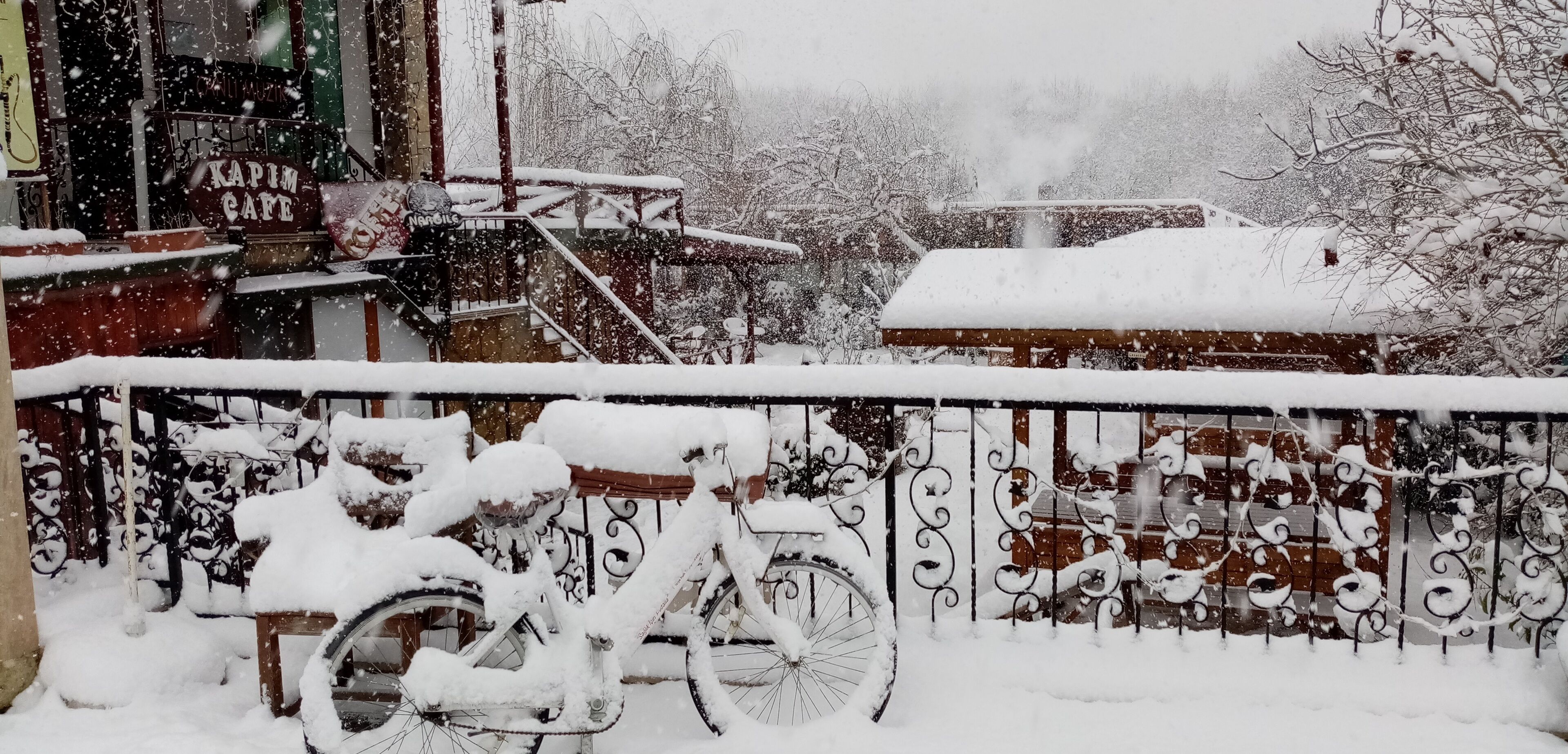 A snow-covered scene with a bicycle parked in front of a building with a sign that reads "KAPIM CAFE".