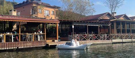 A waterfront restaurant with outdoor seating, a dock, and a boat.