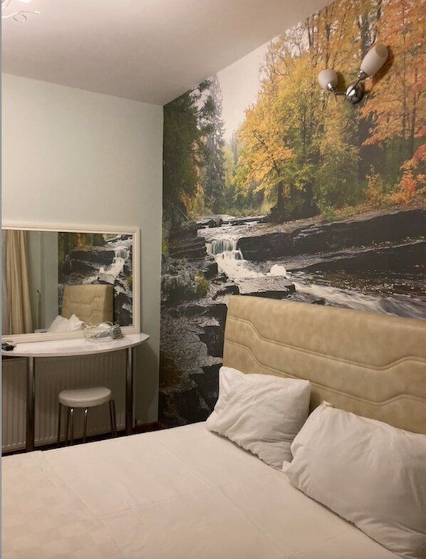 Een hotelkamer met een bed, een bureau met stoel, een spiegel en een muurschildering van een waterval.