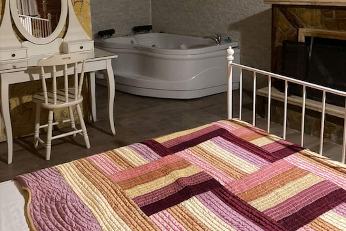 Un dormitorio con cama, escritorio con silla, tocador con espejo y bañera en esquina.