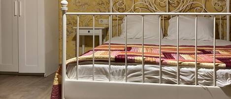 A bedroom with a white metal bed frame, a wooden wardrobe, and a patterned wallpaper.
