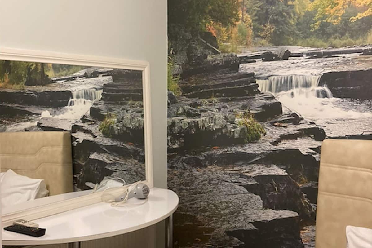 Un baño con un amplio mural de cascada, un lavamanos blanco y un taburete.