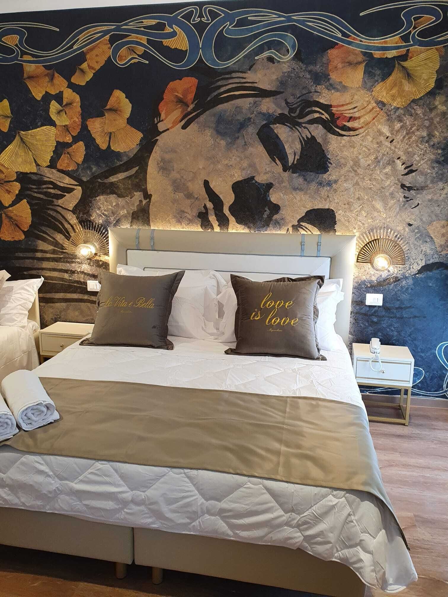 Uma cama com cobertura acolchoada, duas almofadas com texto e uma parede com um mural floral.